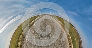 tiny planet transformation with curvature of space among fields on gravel road in sunny day with sky and fluffy clouds