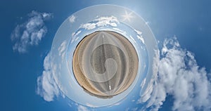 tiny planet transformation with curvature of space among fields on road in sunny day with sky and fluffy clouds