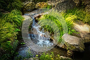 Tiny rivlet waterfall over rocks through tufts of grass with silky slow shutter water