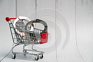 Tiny shopping cart with handcuff on on white wooden background