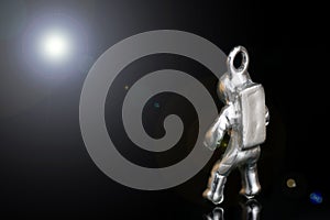 Tiny steel figurine of an astronaut looking at the light of a distant star. Close-up shot, isolated on black, lens flare