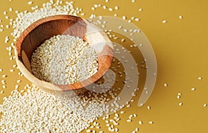 Tiny white sesame seeds in small wooden bowl, on yellow board, closeup photo