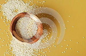 Tiny white sesame seeds in small wooden bowl, on yellow desk, view from above