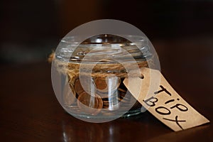 Tip box full of coins on wooden table in cafe, closeup