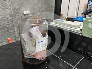 Tip jar on a counter in a coffee shop filled with money.