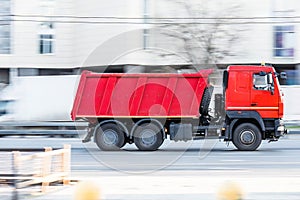 tipper truck is driving in city on high speed. Red dump truck at the city highway in motion