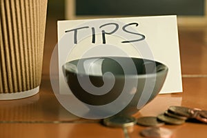 Tipping bowl in coffee shop with coins and coffee cup