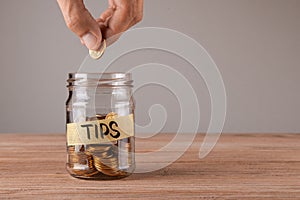 Tips. Glass jar with coins and an inscription tips. Man holds coin