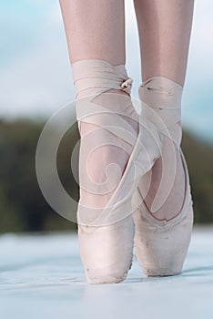 On the tips of the toes. Female feet in pointe shoes. Pointe shoes worn by ballet dancer. Ballerina shoes. Legs in white