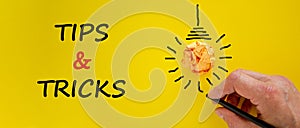 Tips and tricks symbol. Businessman writing words `Tips and tricks`,  on beautiful yellow background. Light bulb icon.