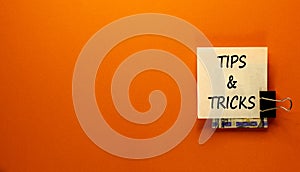 Tips and tricks symbol. White paper clip with dollars cash money. Words `Tips and tricks`. Beautiful orange background. Business