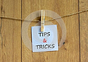 Tips and tricks symbol. White paper on wooden clothespin. Words `Tips and tricks`. Beautiful wooden background. Business and tip