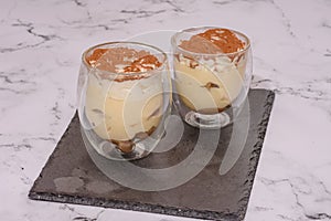 Tiramisu In A Glass Container Against A White Marble Countertop
