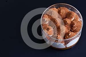 Tiramisu in a glass dome on black background layers sprinkling