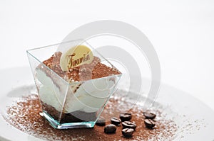 Tiramisu in taster with cocoa powder and coffee beans on white plate, italian desserts, patisserie, italian gastronomy, photograph