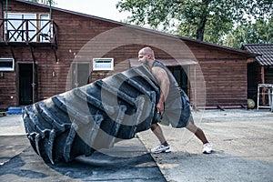 Tire flip exercise. Bald sportsman is engaged in workout with heavy tire in street gym. Concept lifting, workout training