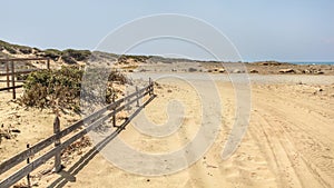 Tire and foot prints on a road leading to beach covered in sand. Sea in distant background