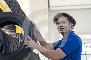Tire shop. Smiling auto mechanic holding tire in tire store