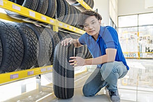 Tire shop. Smiling auto mechanic holding tire in tire store