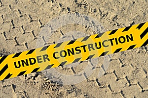 Tire track in a sand with under construction yellow tape