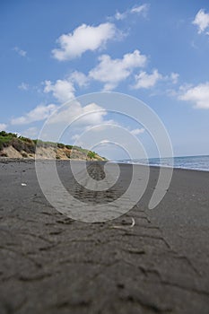 Tire tracks on the sand of a beach with a blue sky