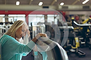 Tired active senior woman wiping sweat towel in fitness studio