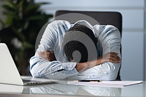 Tired african american businessman sleeping at workplace in office.