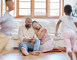 Tired African American couple sitting on the lounge floor looking tired and drained while their hyper children plays