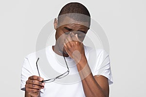Tired african american man massaging nose bridge taking off glasses