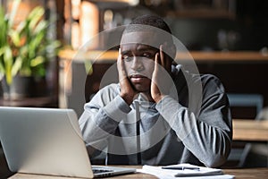 Tired African American man working on laptop in coffeehouse photo