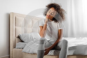 Tired african american millennial woman touching aching neck in bedroom