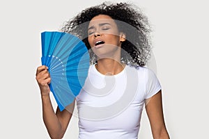 Tired African American woman suffering from heat, waving fan