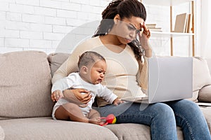 Tired African Mother With Crying Baby Using Laptop At Home