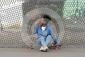 Tired afro american skateboarder girl refreshing after longboarding sit on skate drink soda beverage