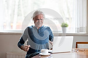 Tired aged man stretching in chair suffering from back pain