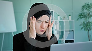 Tired Arabian Muslim Islamic woman in black hijab female worker student take short pause in online work feeling headache