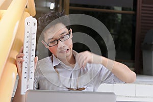 Tired Asian business man with thermometer sitting and sweating after work. Summer heat day concept.