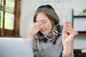 Tired Asian businesswoman taking off her eyeglasses, headache or eyes strain