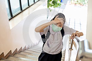 Tired asian child girl suffering from headache migraine,touches head or forehead with hand while walking up the stairs at school,