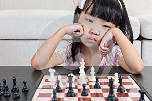 Tired Asian Chinese little girl playing chess at home