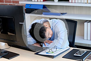 Tired asian man sleeping at office desk. Young businessman with eyeglasses overworked and fell asleep, Creative casual man