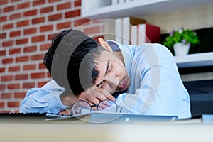 Tired asian man sleeping at office desk. Young businessman with eyeglasses overworked and fell asleep, Creative casual man