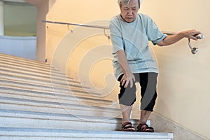 Tired asian senior woman going down the stairs with leg pain,touch her knee pain,female elderly with acute knee joint pain,