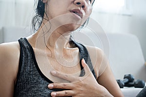 Tired Asian woman having heart attack after doing sport hand holding her chest pain that sweat from overtraining