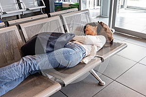 Tired Asian woman lie down sleeping flat on airport departure waiting area chairs while waiting for flight