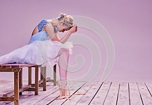 Tired ballet dancer sitting on the wooden floor