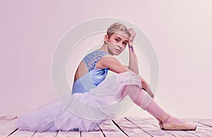 Tired ballet dancer sitting on the wooden floor