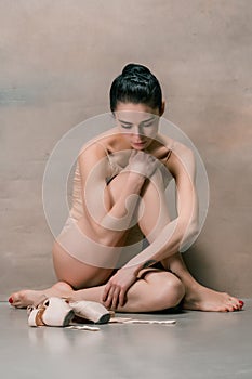 Tired ballet dancer sitting on the wooden floor on a pink background