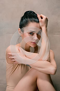 Tired ballet dancer sitting on the wooden floor on a pink background