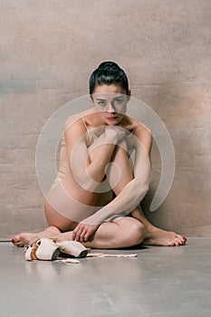 Tired ballet dancer sitting on the wooden floor on a pink background